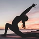 Outdoor yoga at sunset near water—person in low lunge pose with arms extended overhead, silhouetted against vibrant pink, orange, and purple sky. Ideal for wellness, mindfulness, and nature-inspired fitness themes.
